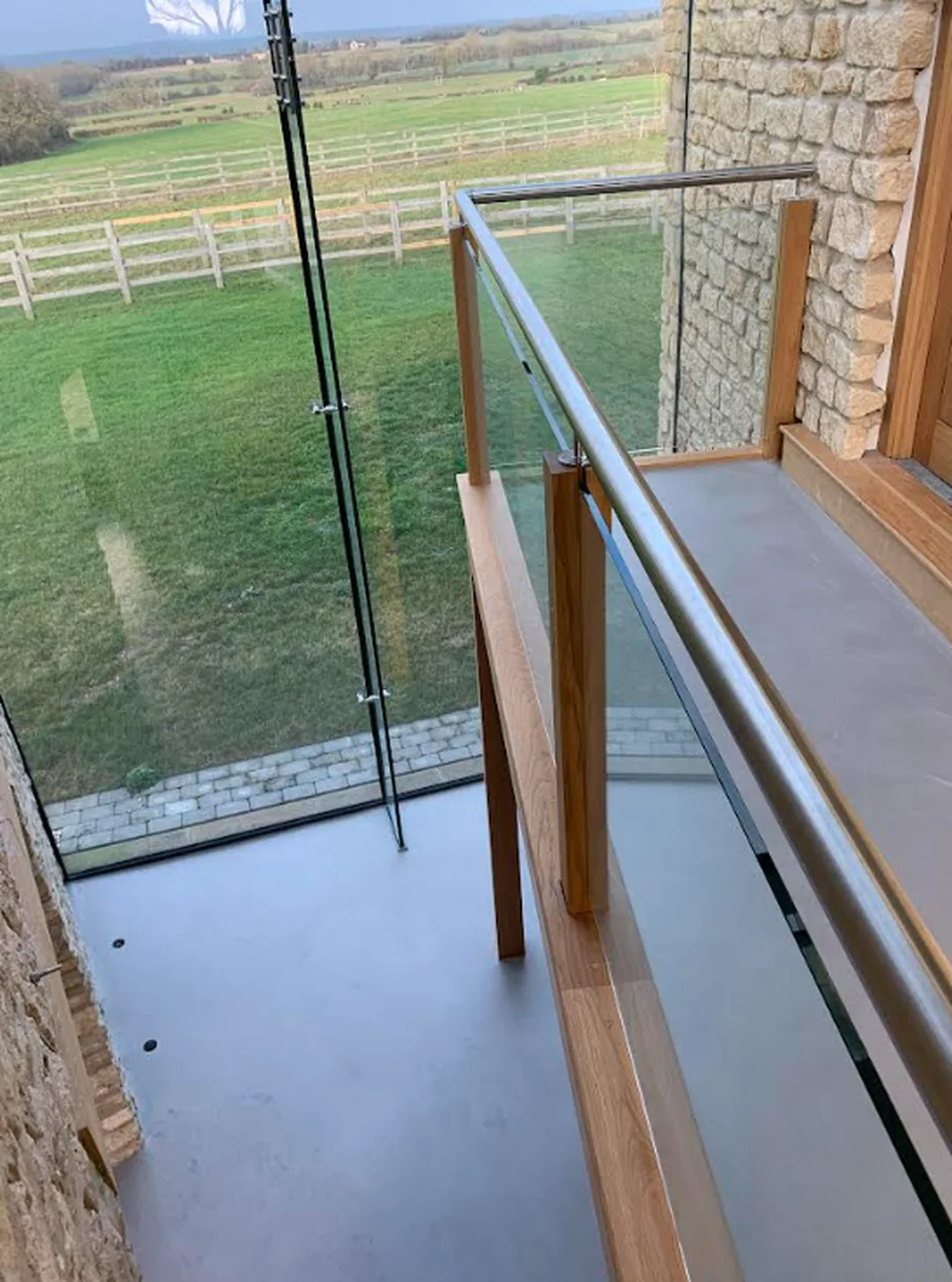 Microcement landing floor beside a glass balustrade in a barn conversion