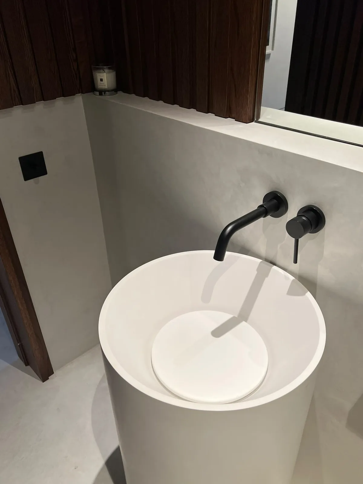 Microcement bathroom wall behind a freestanding basin with wall-mounted taps