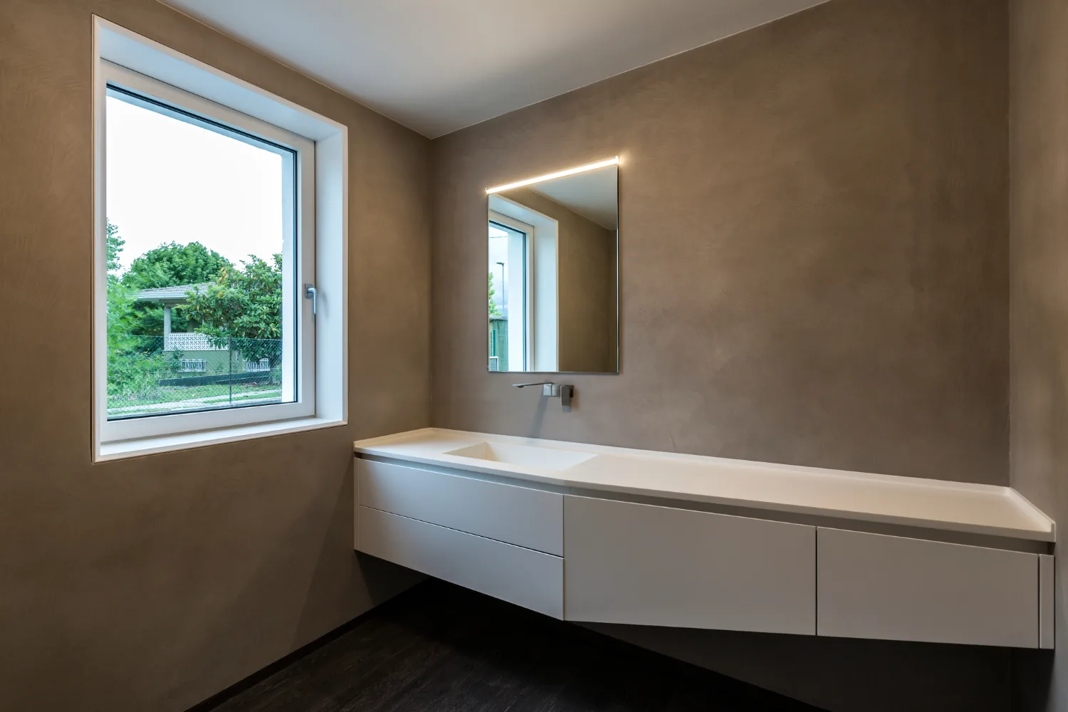 Warm microcement bathroom walls around a floating vanity unit with a mirror