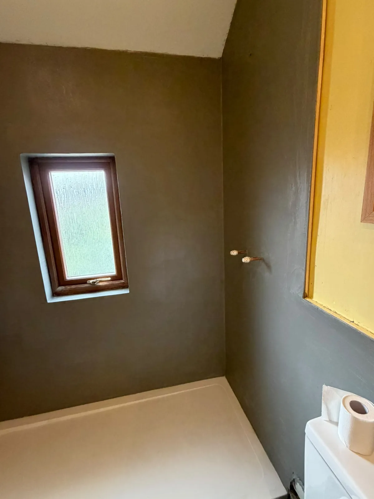 Warm grey microcement shower walls beside a bathroom window