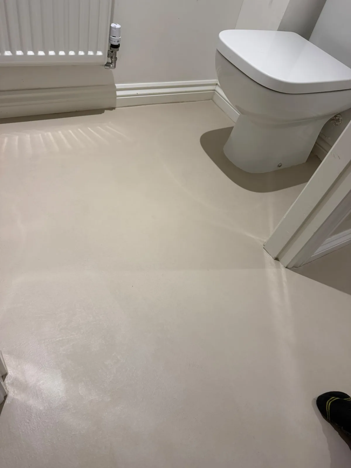 Cream microcement bathroom floor laid joint-free around the sanitaryware